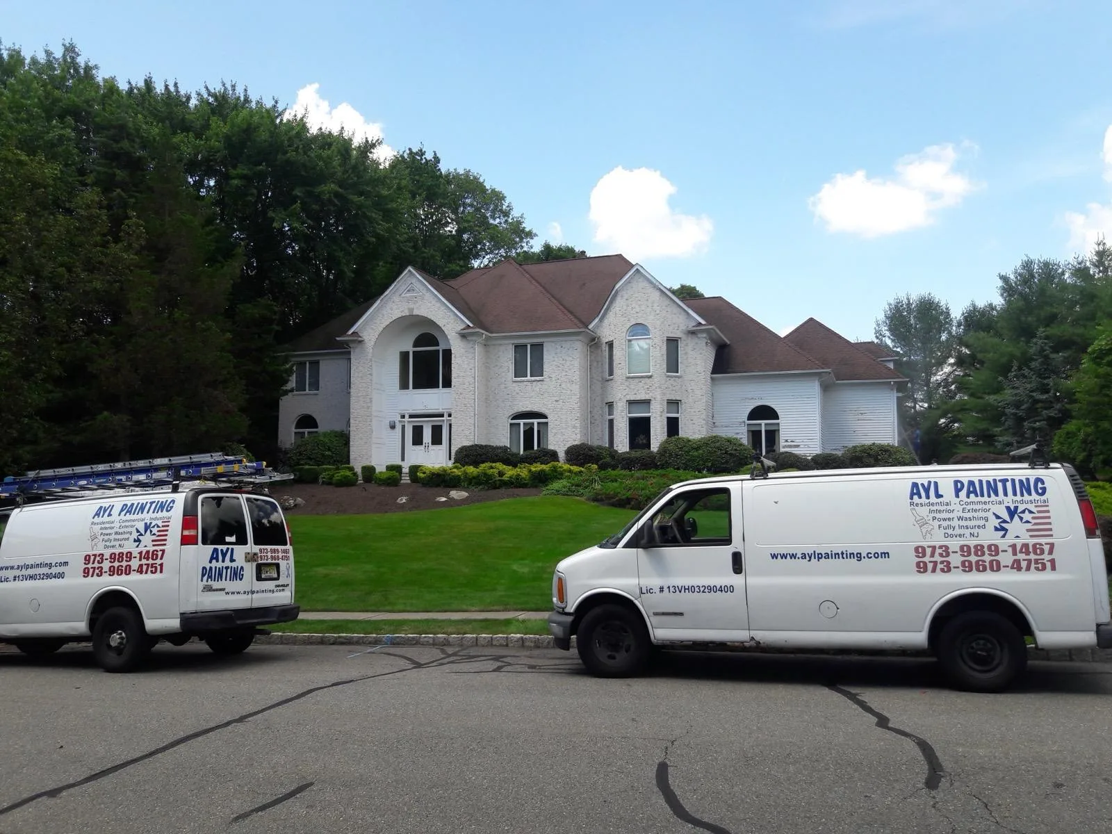 Two A.Y.L. Painting vans with ladders on their roof racks parked outside a large white brick home.