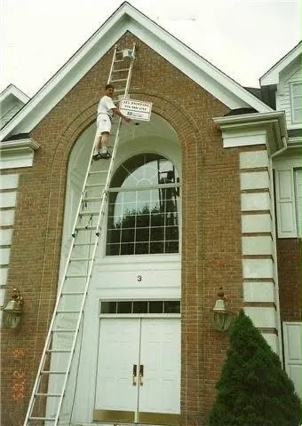 A painter on an extension ladder working on the arched brick entry of a church, with an A.Y.L. Painting sign hung from the ladder.