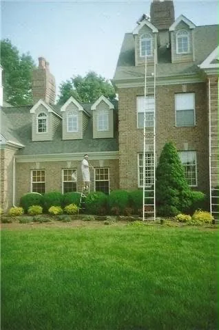 A large brick house with dormers, an extension ladder set against the upper storey and a painter working below it.