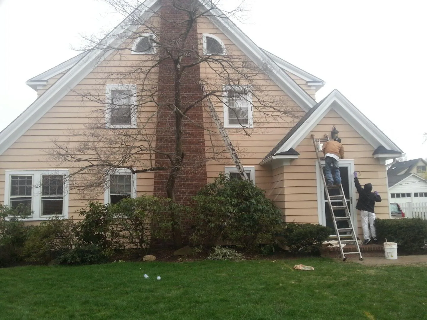 Two painters working on the siding and entry of a house, one from a ladder.