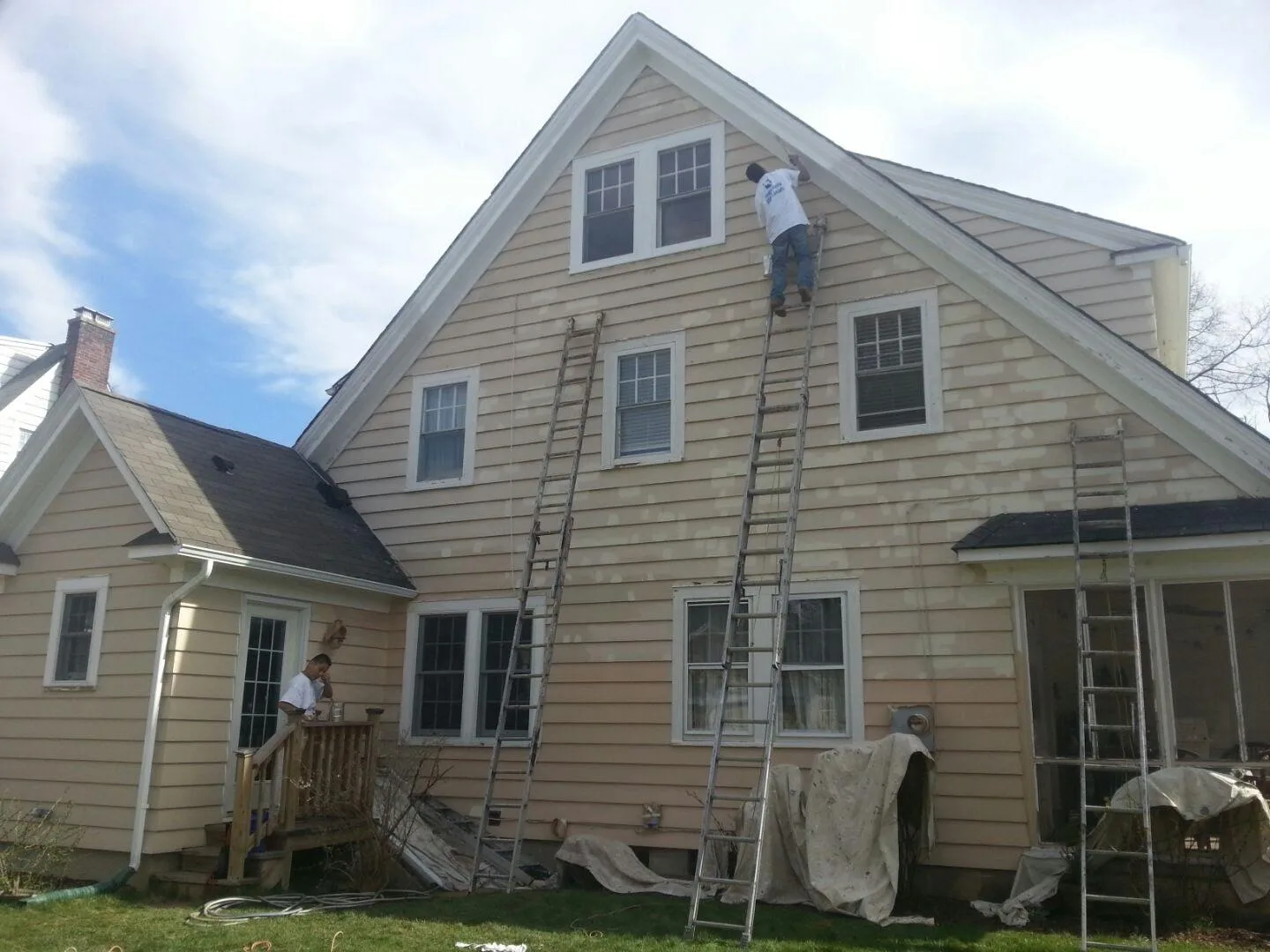 A painter on an extension ladder working on the upper siding and trim of a house.