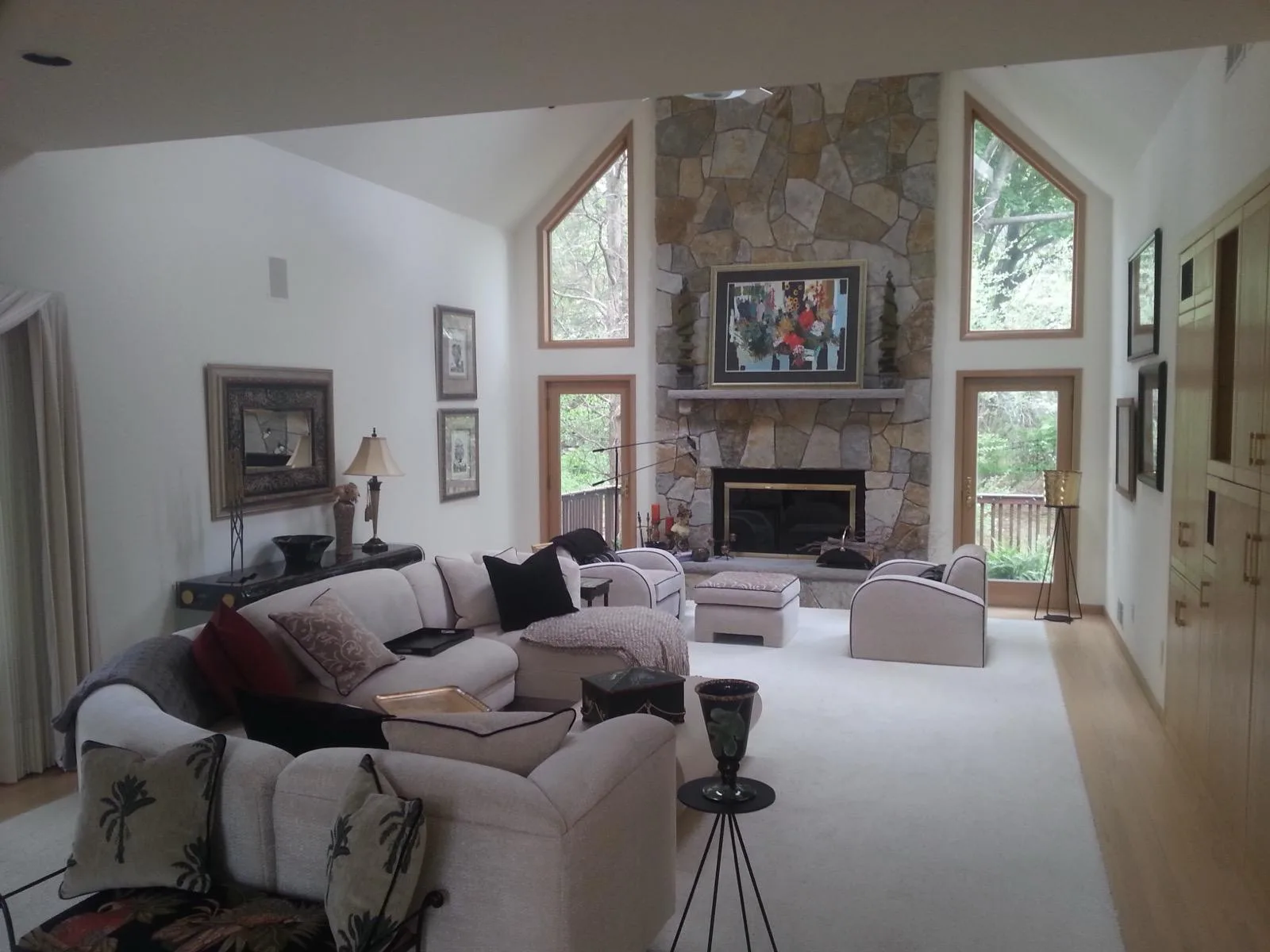 A finished living room with white walls, a vaulted ceiling and a full-height stone fireplace.