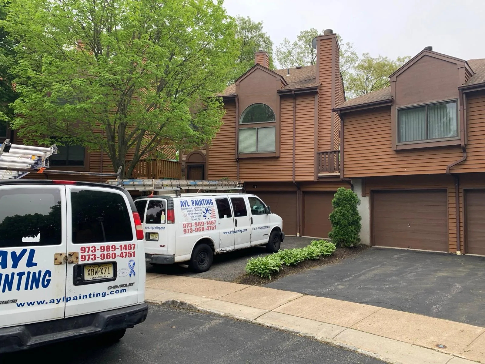 Two A.Y.L. Painting vans parked outside brown-sided multi-unit residential buildings.