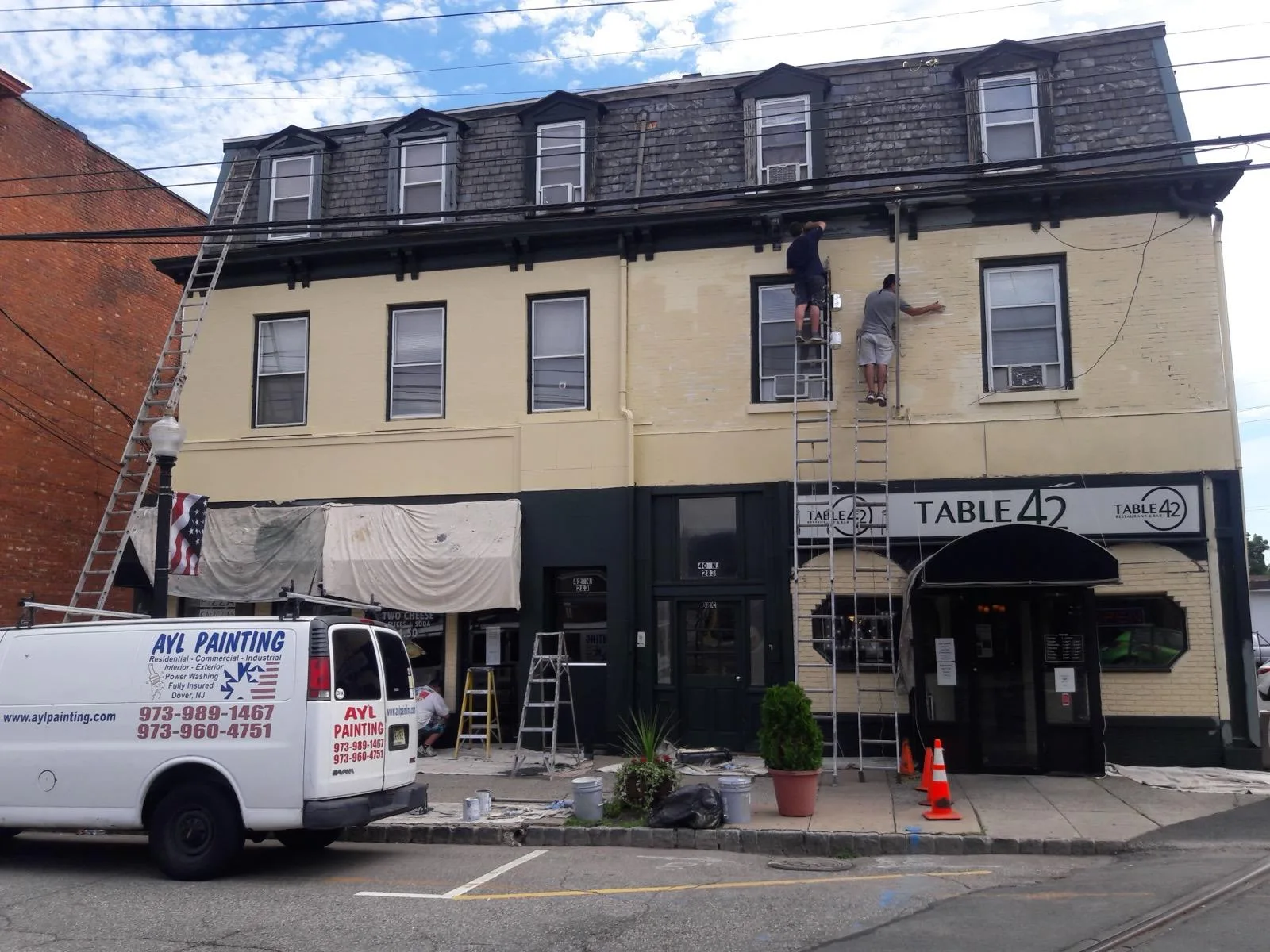 Two A.Y.L. painters on extension ladders painting the upper facade of the Table 42 restaurant building.